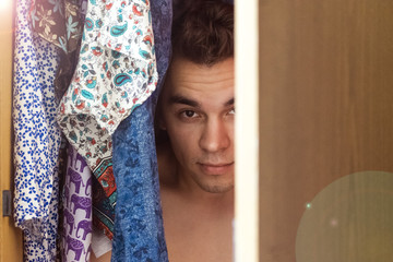 A young man hiding in the closet among women's clothing. Lover in the closet.