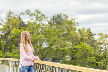 Naklejka na ściany i meble Blonde funny happy pretty girl in a pink sweatshirt on the bridge in park. Sunny day.