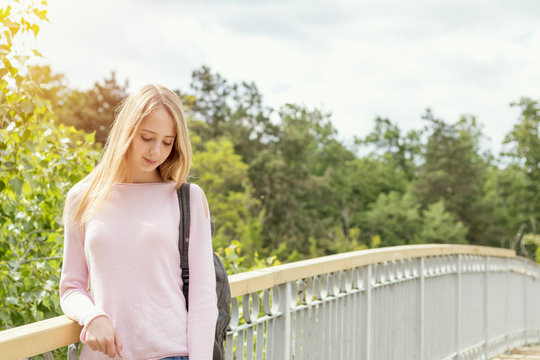 Blonde funny happy pretty girl in a pink sweatshirt on the bridge in park. Sunny day.