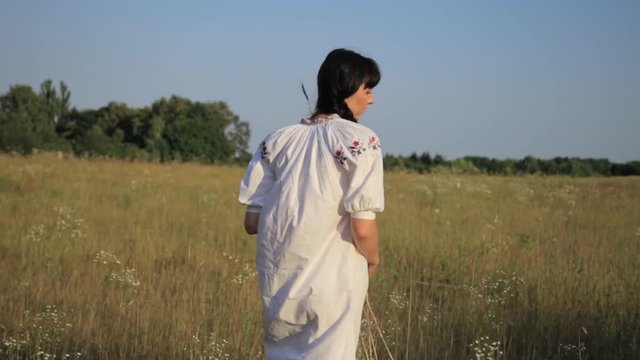 Girl gathering flowers to make circlet at sunset in summer meadow nature.