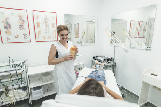 Young woman in beauty center ready for treatment, smiling and looking at doctor