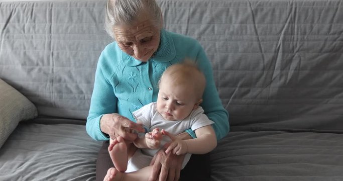 An old grandmother with gray hair and deep wrinkles holds a grandson in her arms.