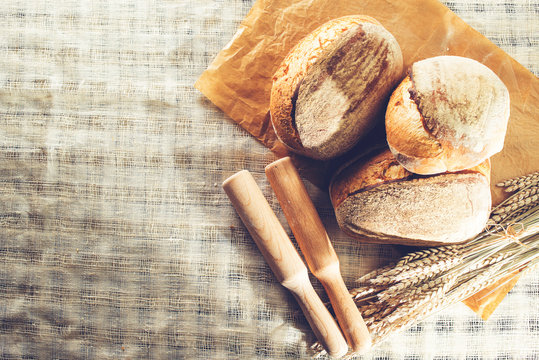 still life with a traditional round artisan wheat bread loaves, wheat and pestles on light textile background. Shallow dof, flat lay, toned image, copyspace fot text