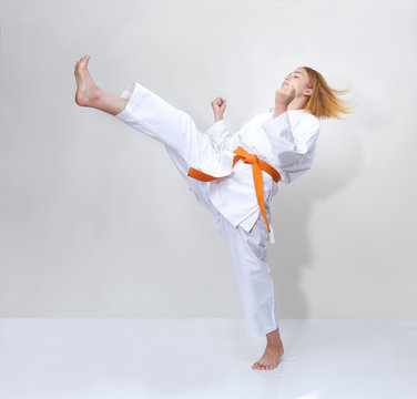 Sportswoman with an orange belt beats a kick on a gray background