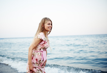Fototapeta na wymiar Pretty smiling female in floral dress running on seashore at sunset. 