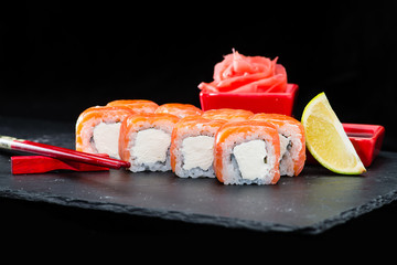 Traditional Japanese cuisine. Selective focus on sushi rolls with salmon, cream cheese, rice and lime on dark background, near ginger and lime