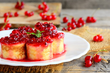 Sweet crepes sushi rolls with redcurrant confiture on a white plate and a vintage wooden table. Stuffed crepes dessert recipe. Easy Easter breakfast idea