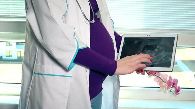 Pregnant female doctor showing her ultrasound photo in tablet computer