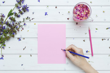 White tabletop scene with female hand writing on a blank pink paper