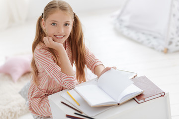 Pretty female youngster smiling into camera while studying