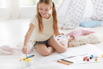 Talented girl sitting on floor and washing brushes while painting