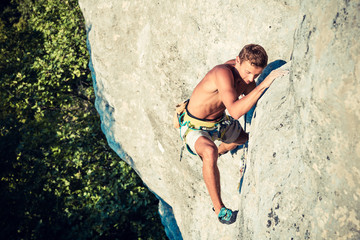 Men climbs an overhanging rock and forest  on the background