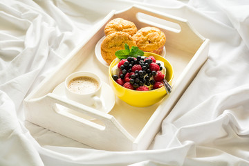 Wooden tray with tasty breakfast on bed. Espresso, banana muffins, cottage cheese with blueberry and raspberry. Sun light. Selective focus
