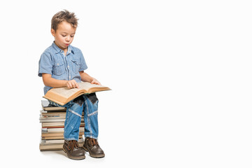 Cute boy in a blue shirt sitting on a pile of books and reading a book on a white background....