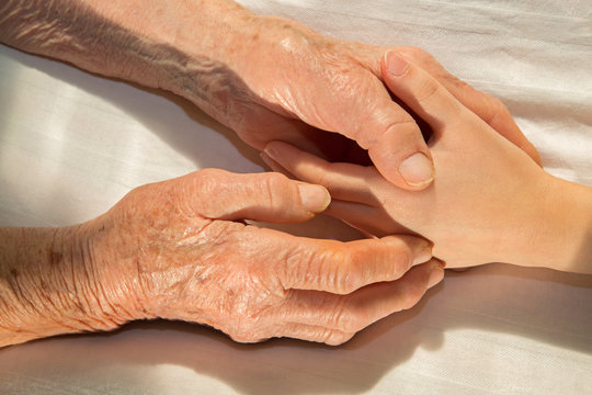 hands of grandmother and grandchild in the bed