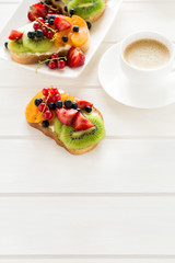 Espresso and fruit dessert sandwiches with ricotta cheese, kiwi, apricot, strawberry, blueberry and red currant on white wooden table. Selective focus