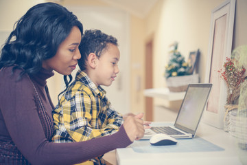 Mother and her son watching something on laptop. African American woman and her son using laptop at home.