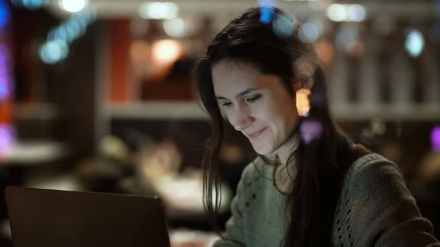 Young happy woman sitting on the cafe and using the laptop. View inside the window on female surfing the Internet.