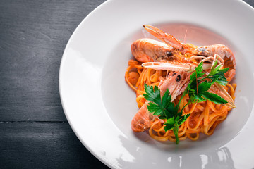 Pasta and tiger shrimp in tomato sauce. Italian traditional food. On a wooden background. Top view. Free space for your text.