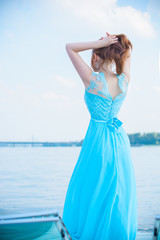 Fototapeta na wymiar Gorgeous woman in long beautiful flying dress. Elegant girl in fluttering dress. Fashion style portrait. Young elegant woman posing at yacht against bridge. Consent of femininity and tenderness