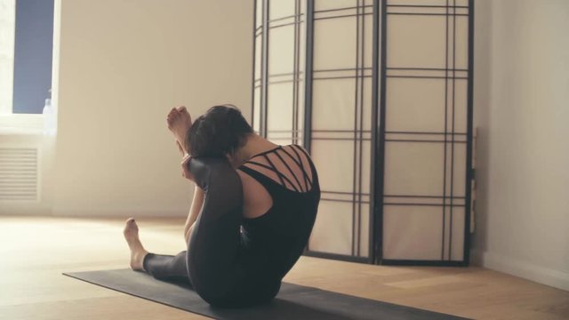 A young woman performing yoga-asanas in the hall.