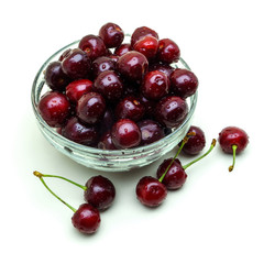 Glass vase with fresh wet cherries on white background