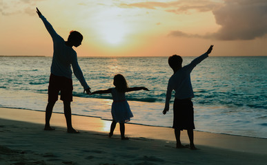 father with son and daughter silhouettes play at sunset beach