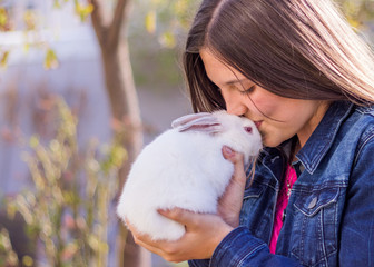 Young teen girl holding a white baby rabbit outdoors kissing it's forehead