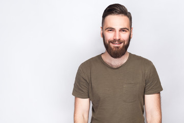 Fototapeta premium Portrait of happy smiley bearded man with dark green t shirt against light gray background. studio shot. .