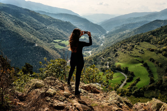 Woman taking pictures with the phone on the top of a mountain