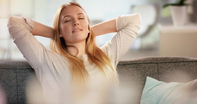Pretty young woman enjoying with eyes closed a me moment on the couch at home