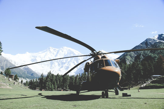 A helicopter parked in pasture between mountains