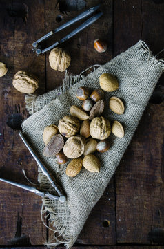 Mixed nuts and nutcrackers on burlap on wood background.