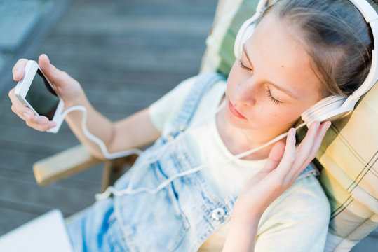Closeup of pretty teen girl in headphones listening to music using a laptop outside on the terrace in the garden