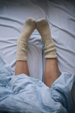 Female legs in cosy winter socks under the sheet on the bed