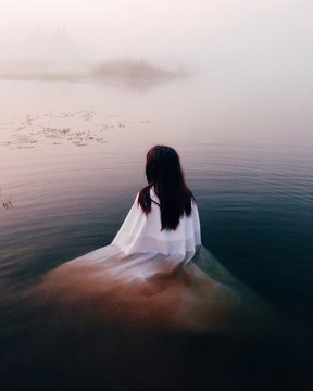 Woman in white dress in lake at sunrise