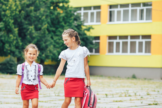 Two beautiful girlfriends girls go to school by the hand. Back to school
