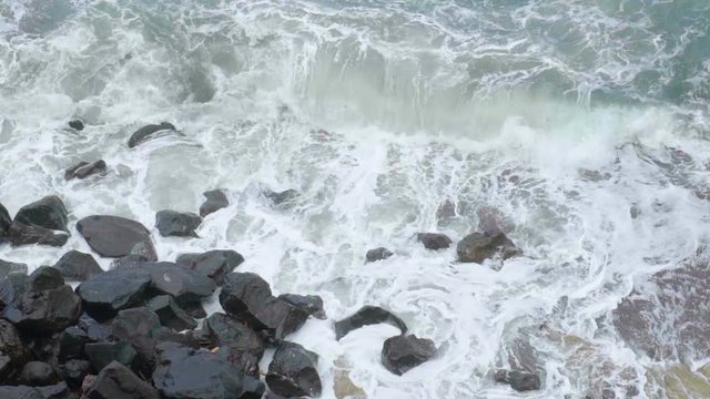 Stormy sea with foamy waves breaking in splashes against cliff, slow motion