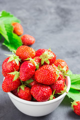 Delicious strawberry in a white bowl on stone background. Selective focus, space for text.