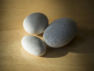 Fototapeta na wymiar three pebbles - white and grey on natural wood desk