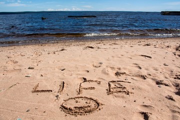 The inscription on the shore of the lake in the sand, against the blue sky and water.