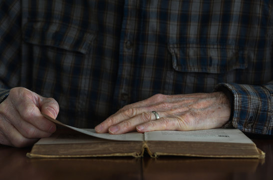 Close-up of a senior man's hands on the pages of an old book.