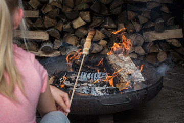 Mädchen von hinten fotografiert am Lagerfeuer mit Stockbrot in der Hand
