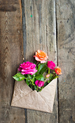 Rose flowers in craft paper envelope over wooden background