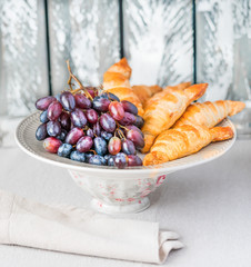 Grapes and croissants on the plate, wooden background