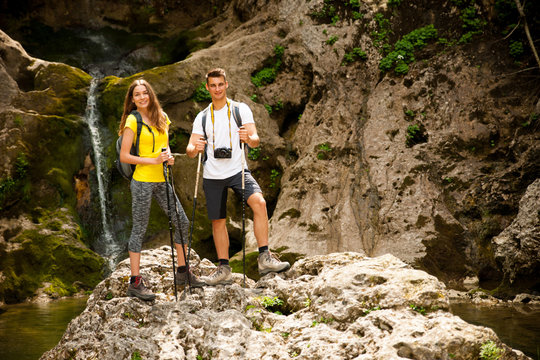 active young couole hiking in nature resting near waterfalll and taking pictures with camera
