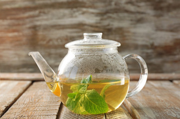 Obraz na płótnie Canvas Glass teapot with hot tasty lemon balm tea on wooden table