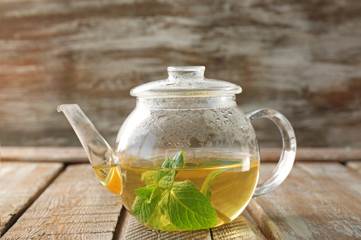 Glass teapot with hot tasty lemon balm tea on wooden table