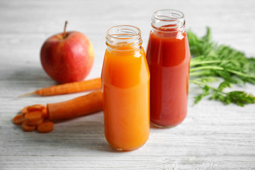 Delicious carrot and tomato juices in bottles on wooden table