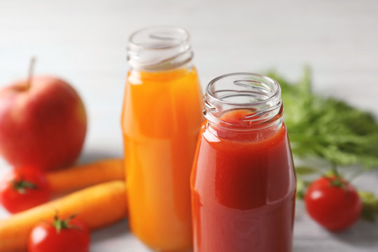 Delicious carrot and tomato juices in bottles on table, closeup